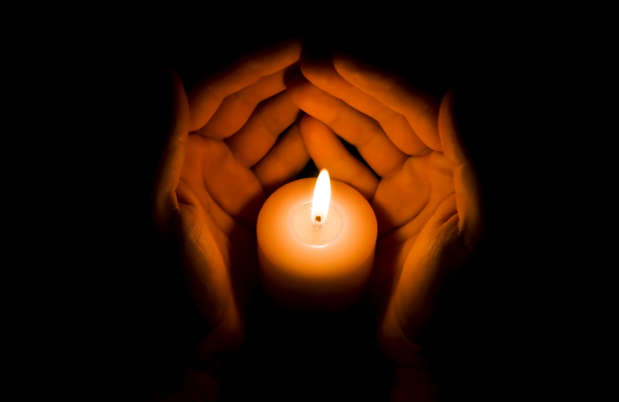 Photo of hands cupped around candle flame