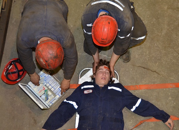 Young worker on stretcher being helped by two other workers